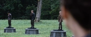 Katniss looks at Peeta, who is standing on the podium between the District 10 male and District 7 female.