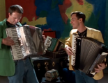 Two men are playing the theme song on accordions by squeezing them.