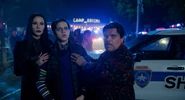 Morticia, Pugsley, and Gomez in front of a police car at Camp Jericho