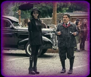 Morticia holding an umbrella while standing next to Gomez