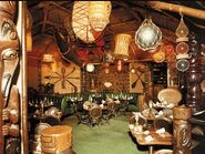 An old tiki restaurant with ropes, nets, glass floats, and rattan furniture.