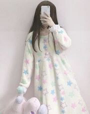 Photo of a girl in a soft dress, the dress has pastel-coloured stars and resembles children's clothing. She is holding a pink and purple stuffed animal horse. She is taking the photo with her phone in front of a mirror, the phone is right in front of her face.
