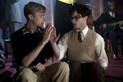 Lucien Carr (Dane DeHaan, Left) and Allen Ginsberg (Daniel Radcliffe, Right), both have their hands held out as if to 'high-five'. Allen's palm is visible to the audience reveling a gash down the center, Lucien is holding the knife they used with his other hand. The characters are performing a 'Blood Oath' while at a party.