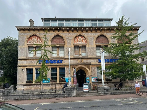The Torquay Museum is an essential stop for those wishing to complete the "Agatha Christie Mile". The plaque is to the left of the entrance between the windows just above a sign which says that the museum is open. In this view it is obscured by a tree.