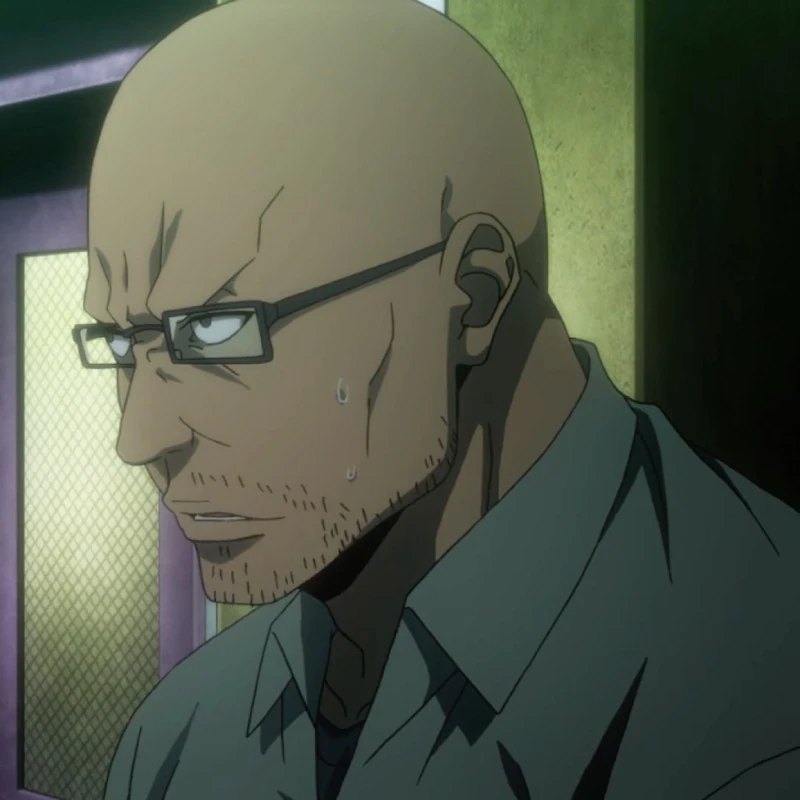 A bald, muscular tanned man with a stubbly beard and reading glasses. He wears a dull buttoned mint collared shirt with a dark grey shirt underneath