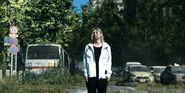 Chishiya standing on an overgrown street, walking between abandoned cars and buses