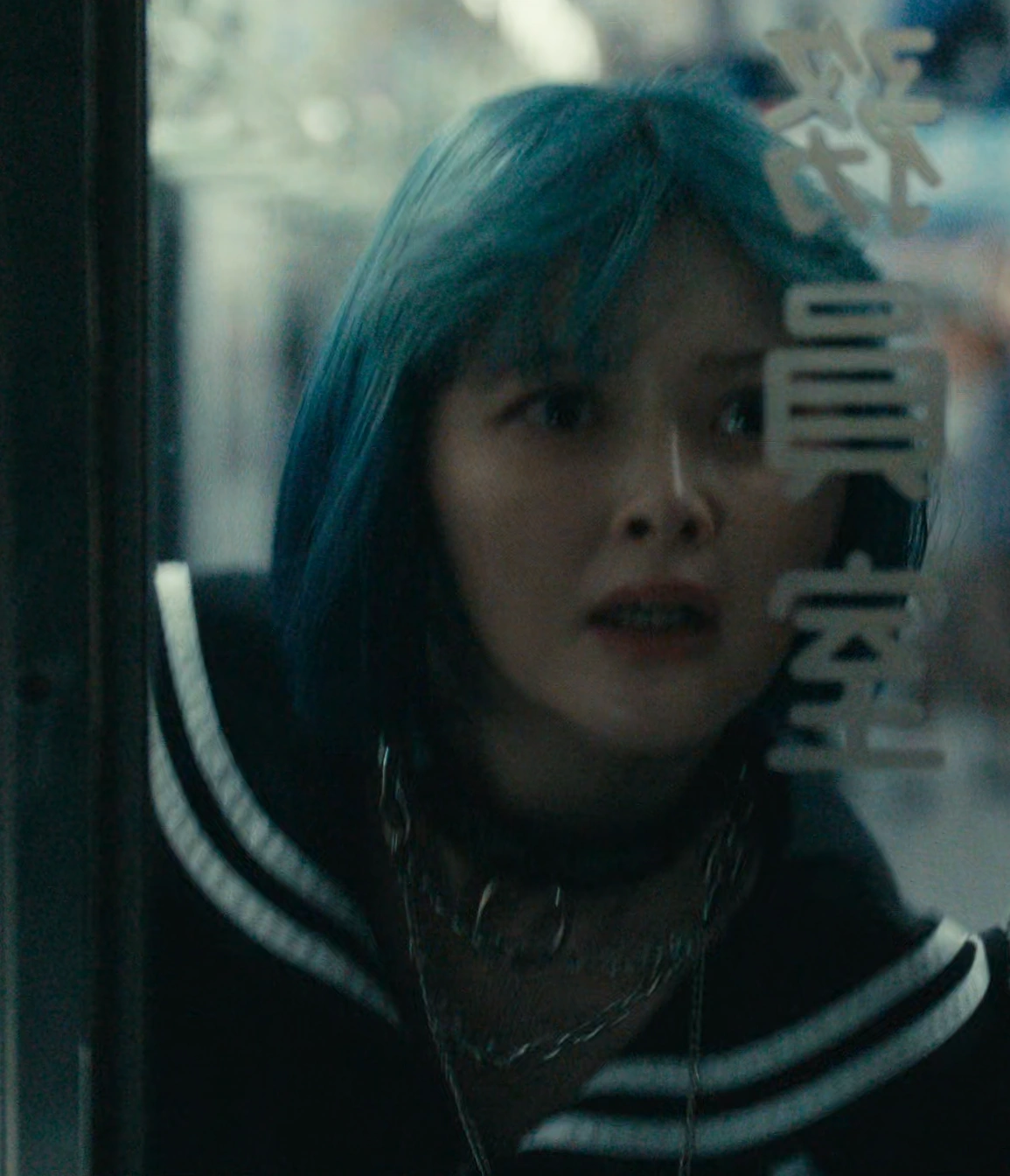 A screenshot of Rei Morikage from Season 3, a young woman with short blue hair in a black hoodie with white stripes, looking through the glass door with a frightened expression