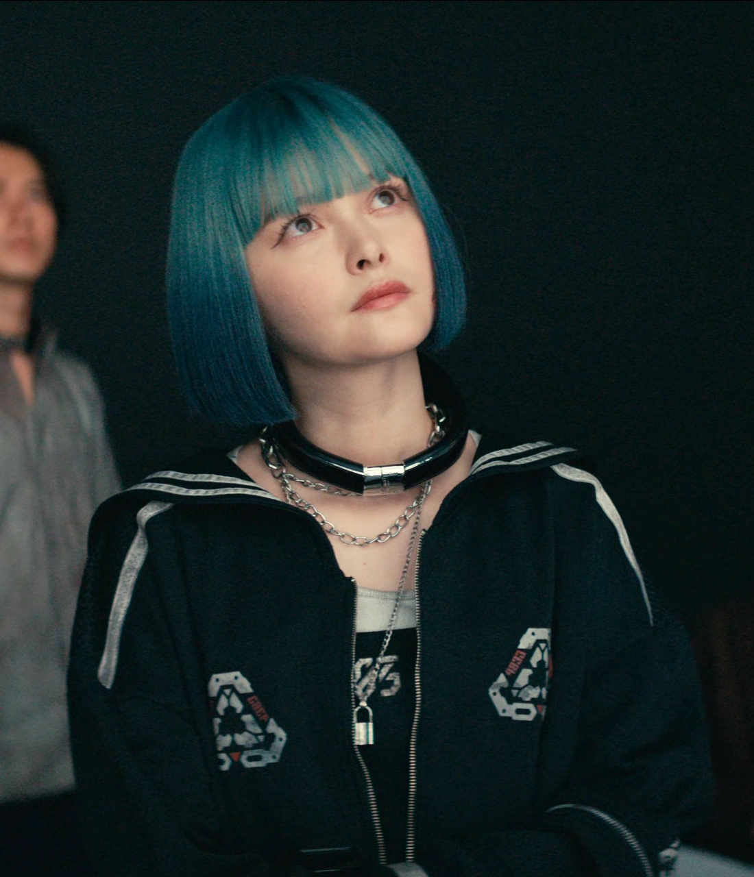 A close-up shot of Rei, looking upwards with a thoughtful expression, a few more players blurred in the background