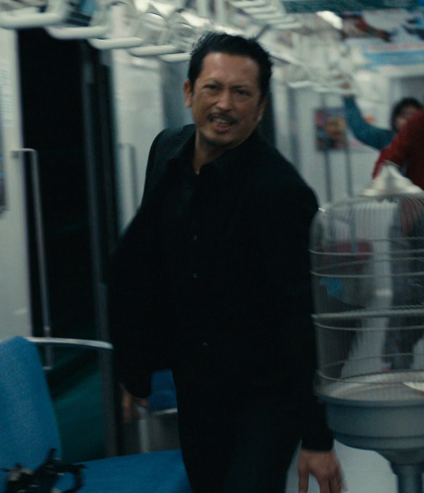 A screenshot of Kazuya from Season 3, a middle-aged man in a black suit, leaning forward with a tense and determined expression