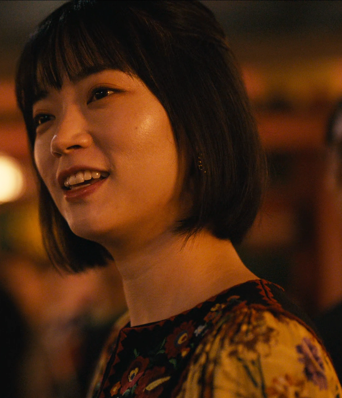 A close-up shot of a smiling young woman with short black hair in a yellow dress with a floral pattern
