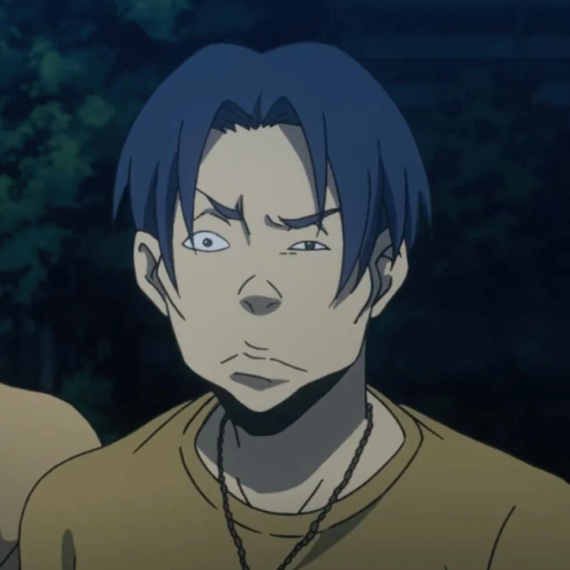 A young man with short, choppy black hair that is parted equally. He wears a dull mustard shirt with a purple butterfly and dog tag necklace