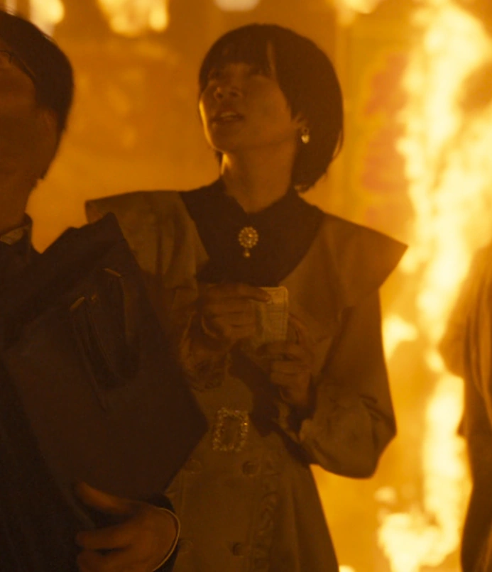 A young woman with short hair, named Rinko in Japanese subtitles, wearing a light gray dress with a wide ruffled collar and earrings, looking at the sky in panic