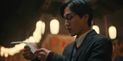Masato holding a fortune slip and reading it closely with sweat on his face