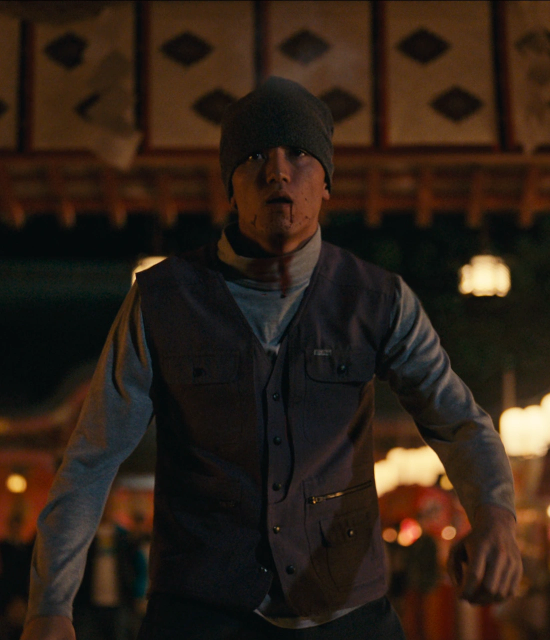 A close-up shot of an older man in a cap and glasses, wearing a gray jacket and looking in front of him with suspicion