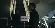 Rei and Kazuya by an escalator with a notice disallowing the entry