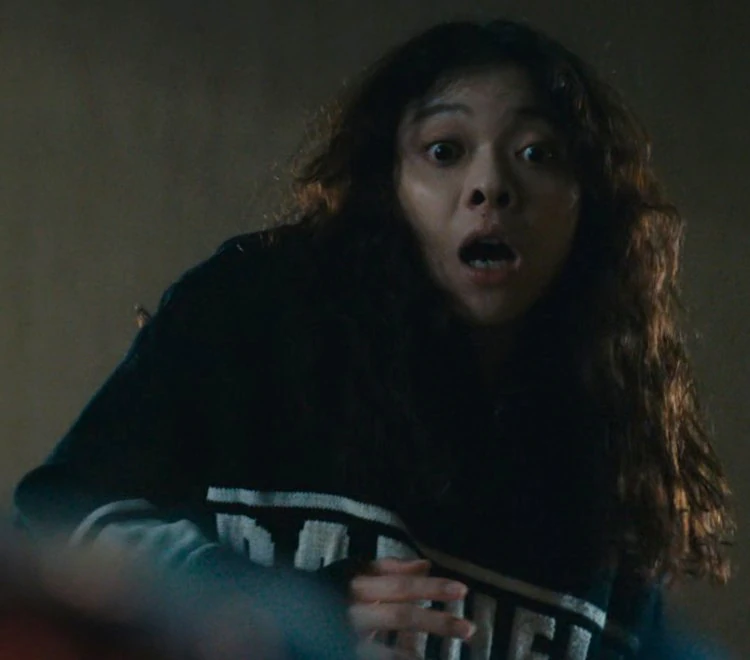 A scared girl with long curly hair, dressed in dark clothes