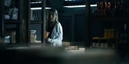 Chishiya standing by the shelf with food and closely observing while holding his own bag of snacks