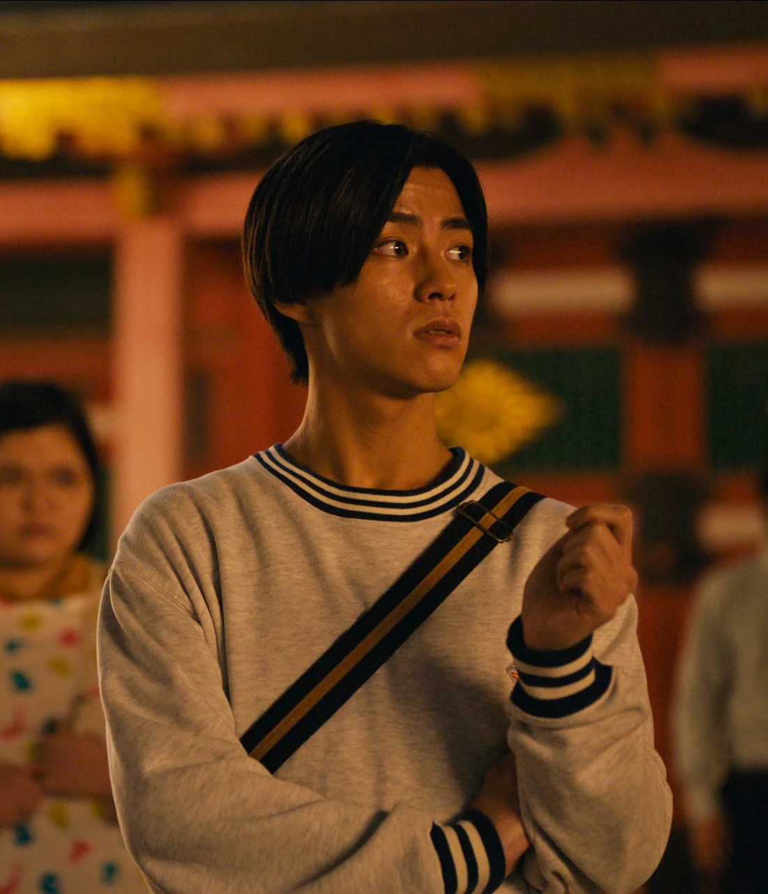 A close-up shot of Nobu in the crowd, looking around the venue, still wearing the clothes from the real world and carrying a bag across his shoulder