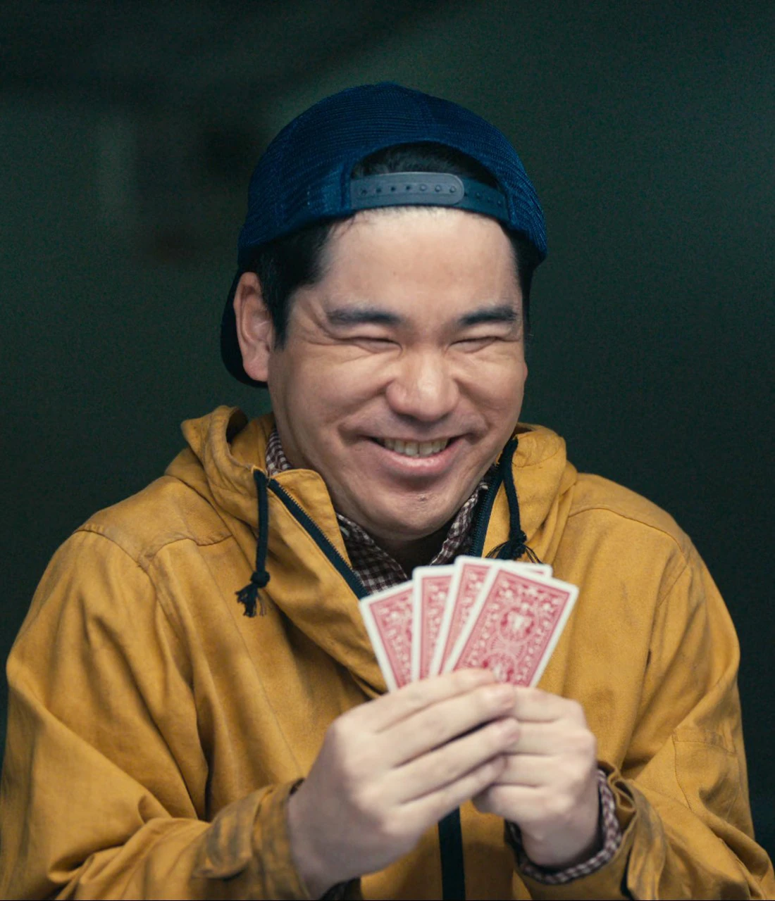 A middle-aged man with a big smile, wearing a yellow jacket and a blue cap
