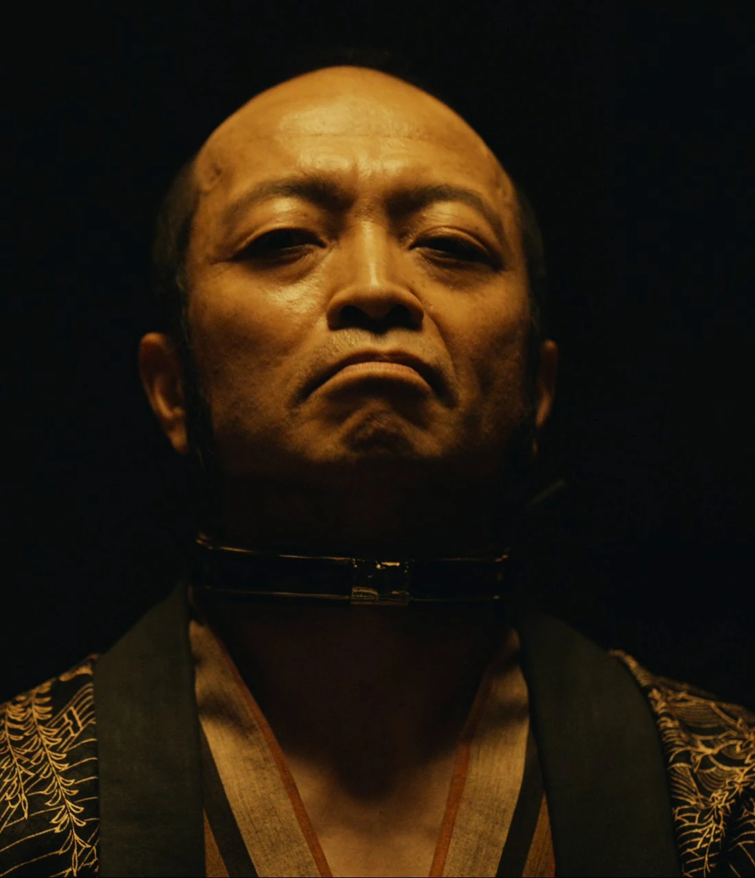 A screenshot of the Jack of Diamonds from Season 2, an bald old man with intense eyes and a tight-lipped, almost scornful expression, who is wearing a traditional clothing