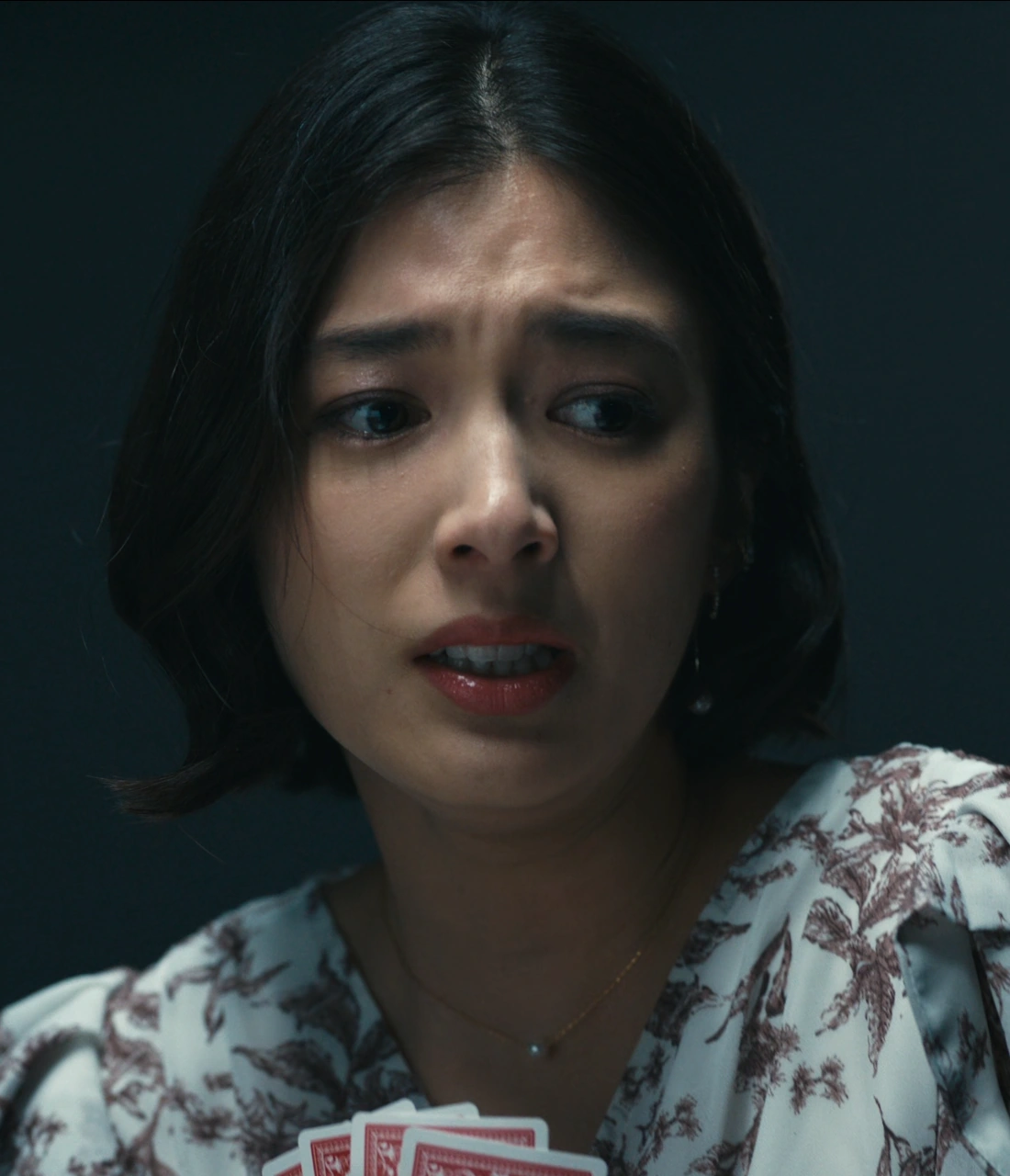 A screenshot of an unnamed player from Season 3, a young woman with short black hair, wearing a light-colored dress with a floral pattern and earrings