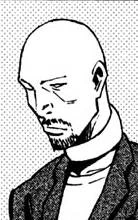 A bald man with a short trimmed beard named Kunio Kariya angled at the right side of the bust image, wearing a dark grey blazer with a white undershirt