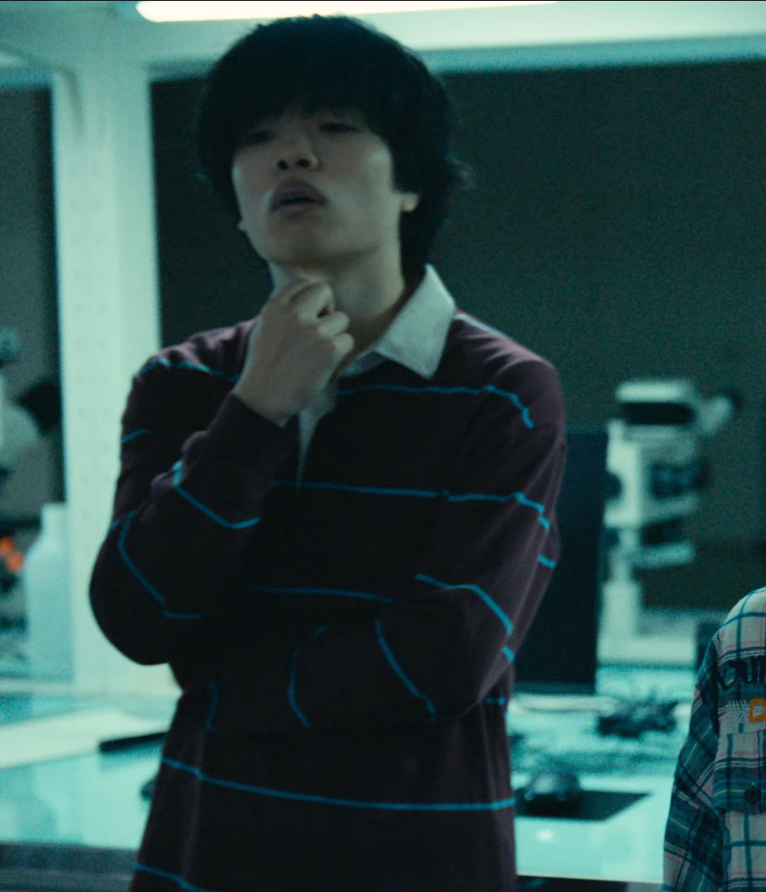A young man, named Yamaoka in the subtitles, with medium-length black hair, wearing a striped red jumper and blue jeans