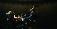 Multiple people in the hall, Kuina mid-air, her foot kicking another player's back, while more participants are about to attack her, holding metal poles