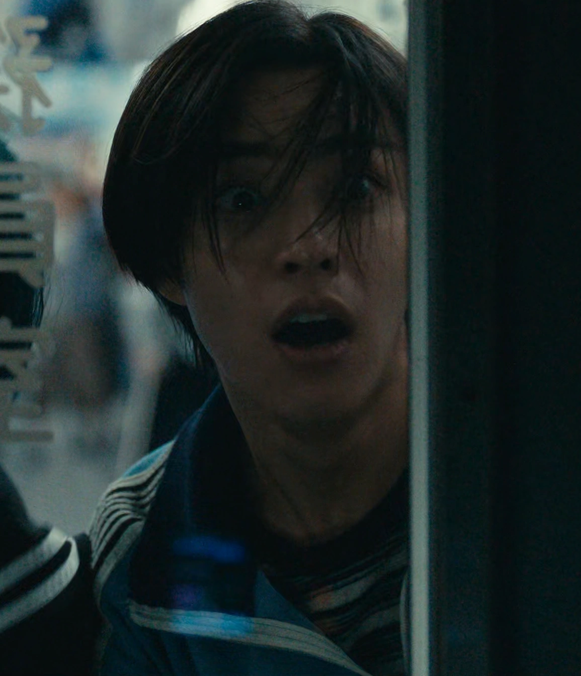 A screenshot of Nobuaki Hida from Season 3, a young man with straight dark hair wearing a blue tracksuit, looking through the glass door with his mouth open in shock