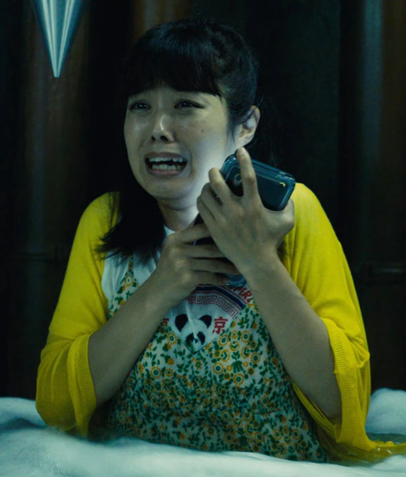 A screenshot of Sakura from Season 1, a woman in a long bright yellow coat, who looks terrified