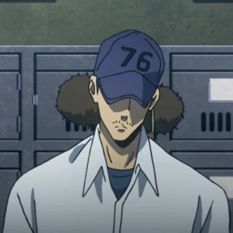 A tanned man with kinky hair in two low buns, wearing a dark blue '76' hat, a gold hoop earring on his left ear, and a white collared shirt over a dull blue one