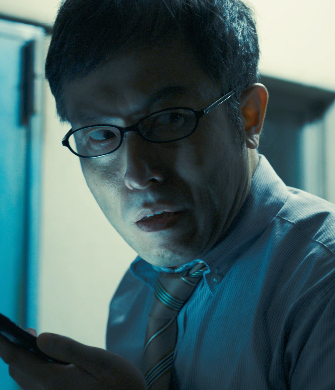 A screenshot of Doi from Season 1, a middle-aged man wearing glasses