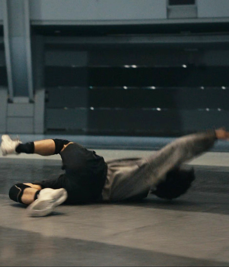 A blurred farway shot of a man with short black hair, wearing a gray shirt, black shorts, and kneepads