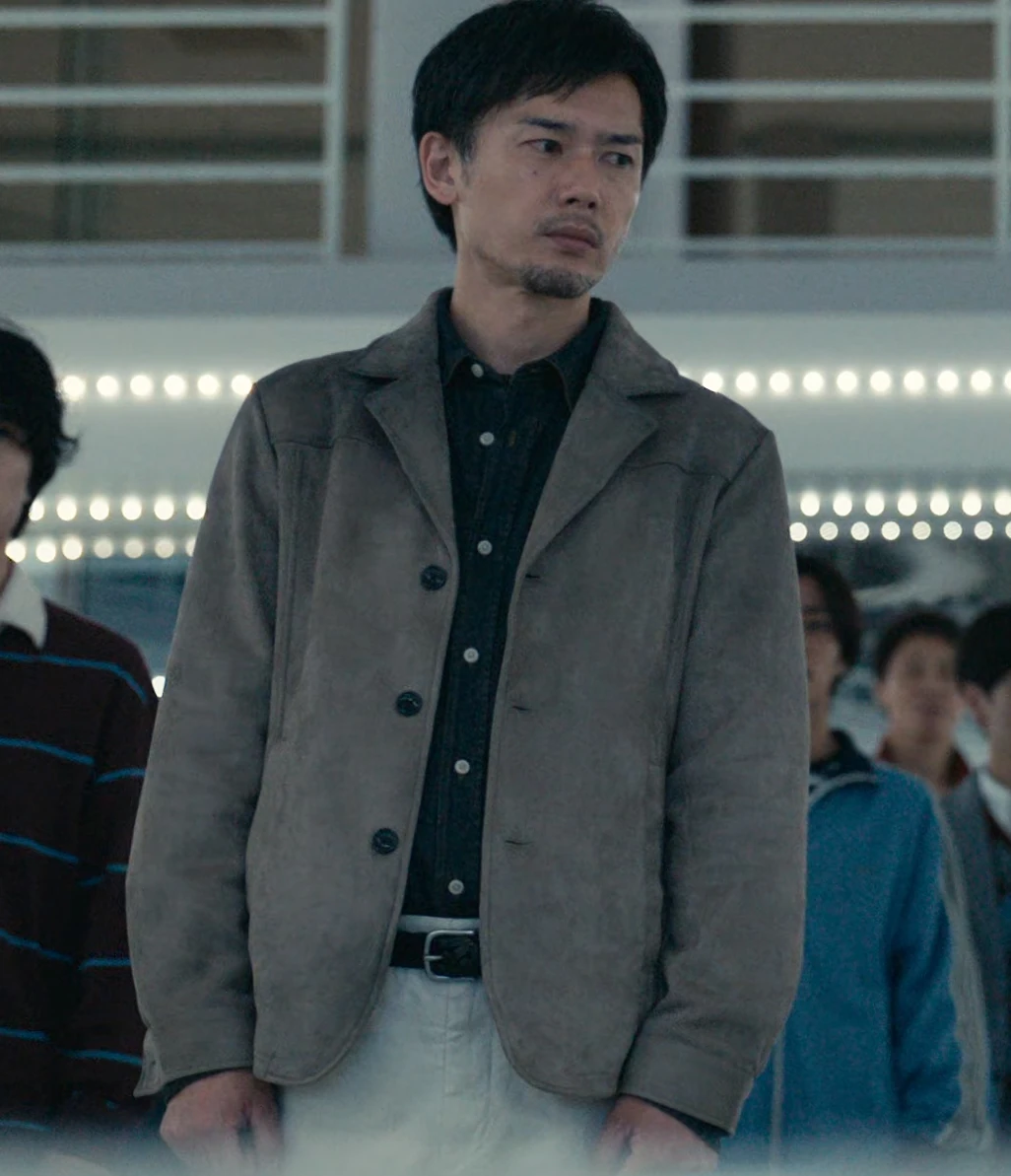 A middle-aged man, named Takahashi in the subtitles, with short black hair and stubble, dressed in formal clothing consisting of a black shirt, a gray jacket suit, and white trousers