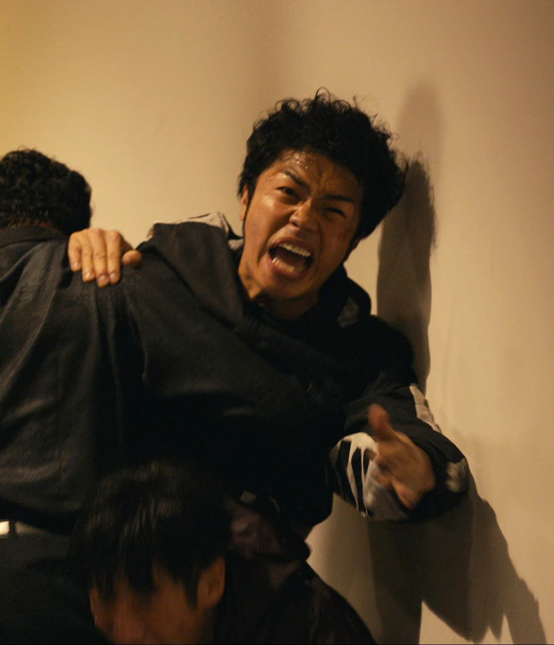 A close-up shot of a man with short curly black hair, wearing a hoodie with white stripes on the sleeves