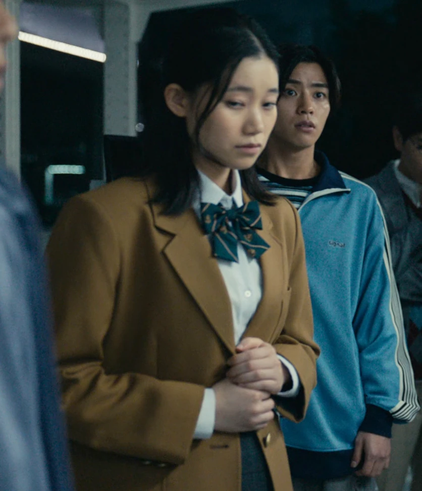 A young woman with medium-length dark hair, dressed in a school uniform with a light-brown cardigan on top