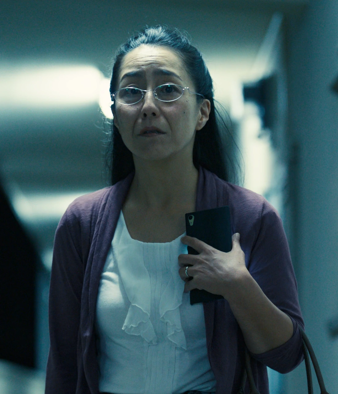 A screenshot of Hirai from Season 1, an older woman in glasses, wearing a purple cardigan