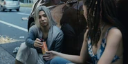 Chishiya and Kuina are hiding behind a car, he is smirking and handing her a soda can with wires