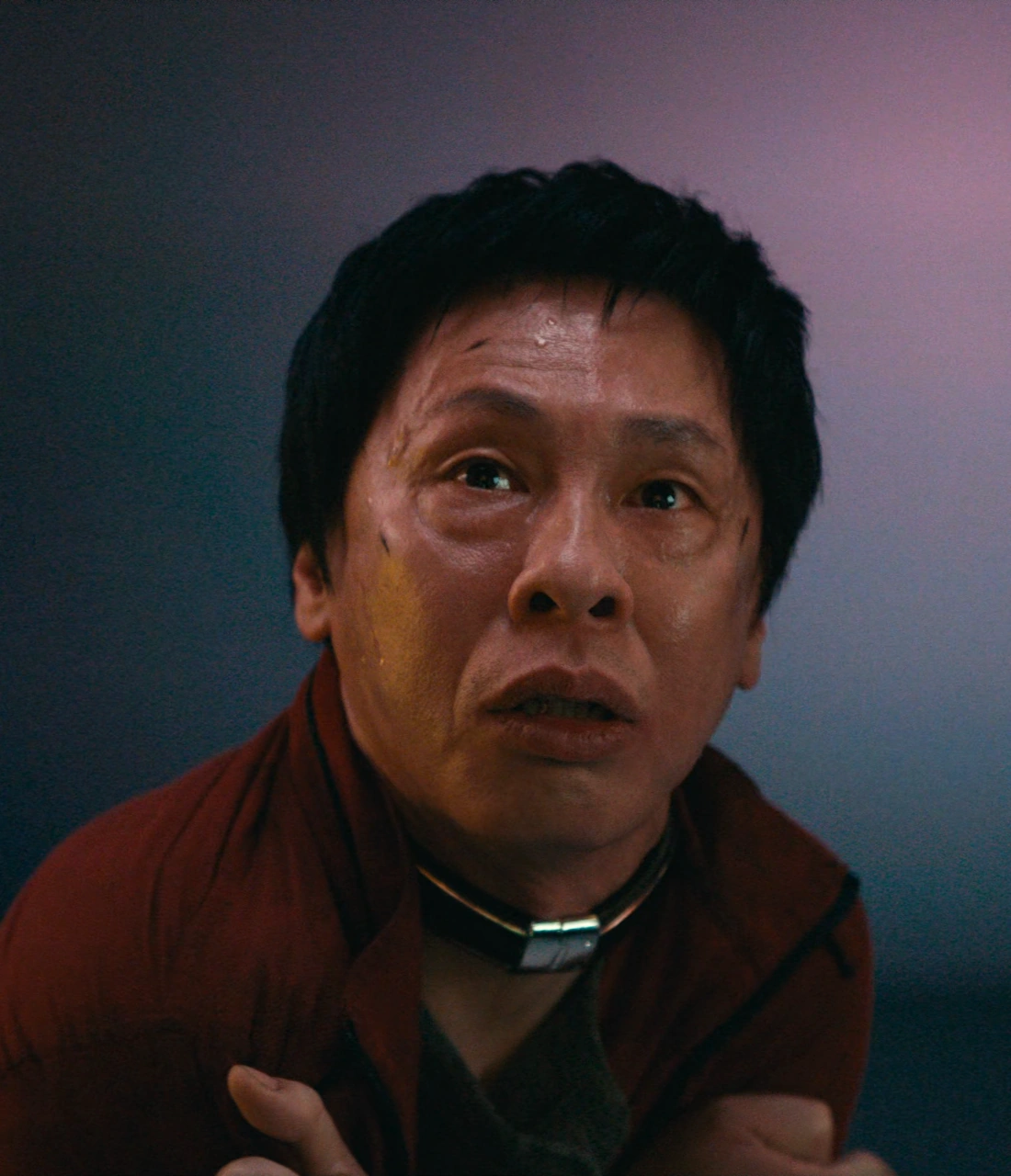 A close-up shot of Tetsu looking up with a frightened expression and embracing himself, his face scratched and sweaty