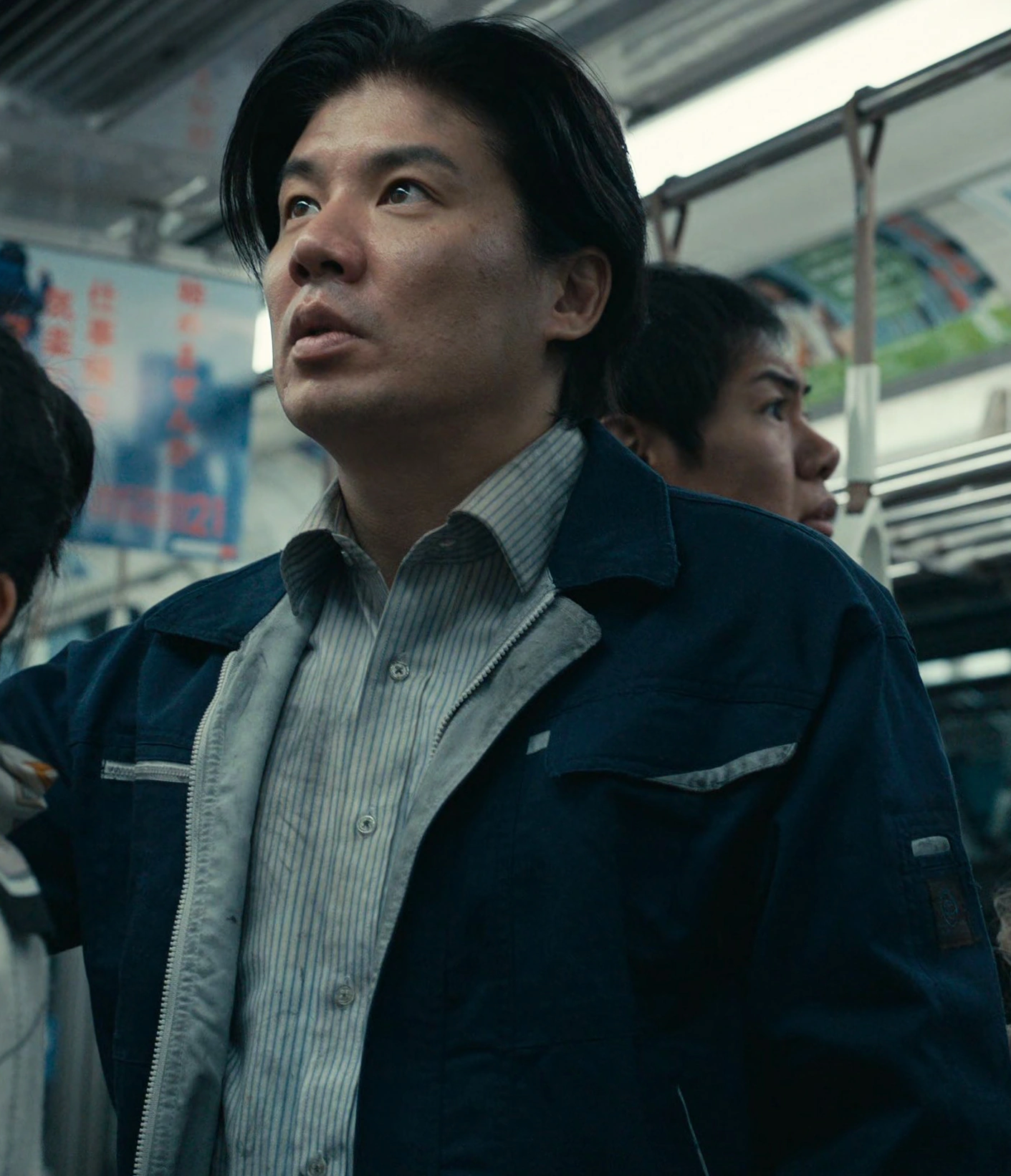 A screenshot of an unnamed male player with straight black hair and long bangs, wearing a blue uniform jacket over a vertically striped shirt