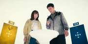 The siblings in a white room with colored doors behind them, Yuna is scared and waiting for her brother to roll the dice