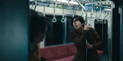 Ryuji grips a pole inside a moving train and looks up tensely, preparing to grab the strap handles