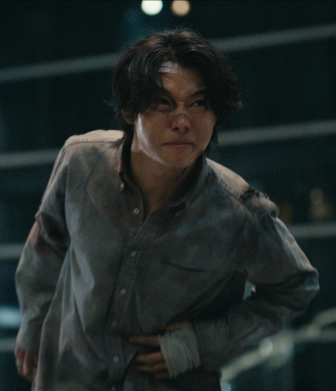 A screenshot of Arisu with his face bruised and his hand bandaged, holding onto his injured side and wincing in pain