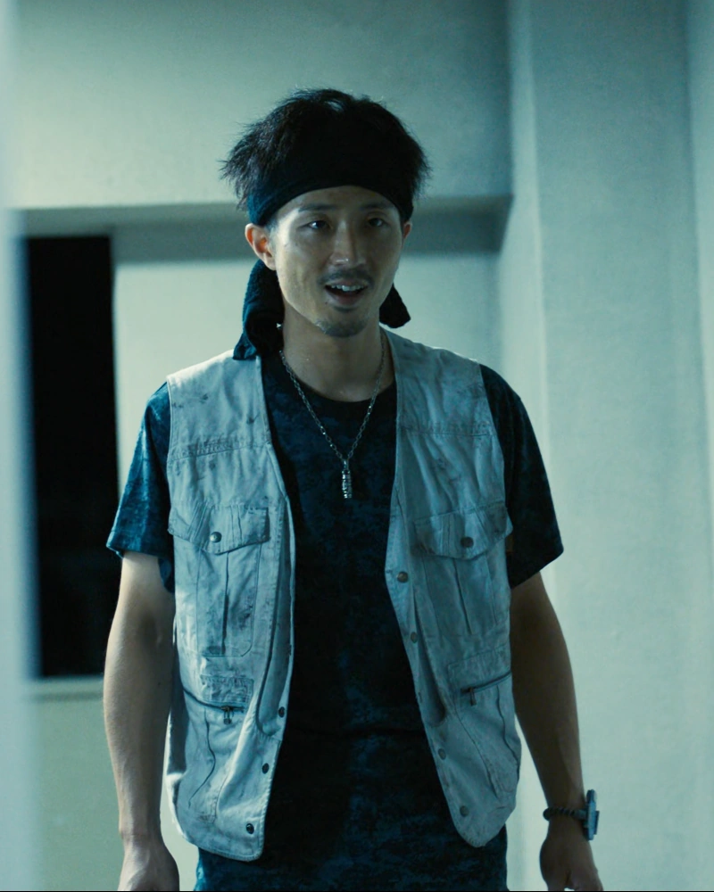 A screenshot of Beach Militant Jin from Season 1, a man with a hairband, wearing a black T-shirt with a white vest on top