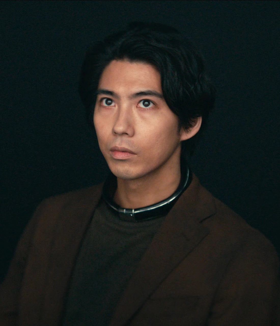A close-up shot of Ryuji looking upwards with a focused expression, wearing a metal collar around his neck