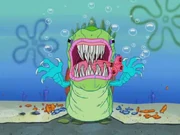 Yellow weaver (bird) with black head hangs an upside-down nest woven out of grass fronds.