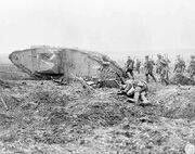 A group of soldiers with guns march on uneven ground past a wrecked tank and the body of another soldier