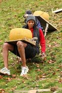 Kisha & Jen struggling to carry cheese wheels down a slippery hill slope during the first leg.