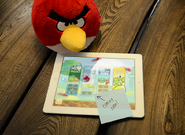 Teaser Photo with a plush Red and an iPad with a blurred level and a sticky tab saying “Coming Soon!”