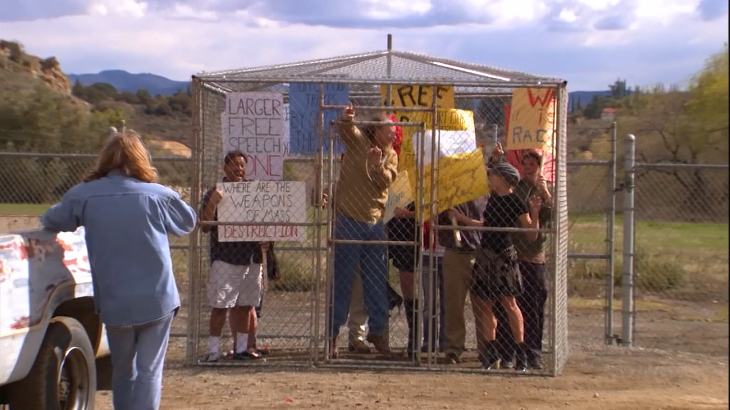 Screen grab of the &quot;Free Speech Zone&quot; from Arrested Development season 1, episode 20: &quot;Whistler&#39;s Mother&quot;. It is a fenced in cage in the middle of nowhere where protests are allowed to occur. A protester inside holds a placard: &quot;LARGER FREE SPEECH ZONE&quot;.